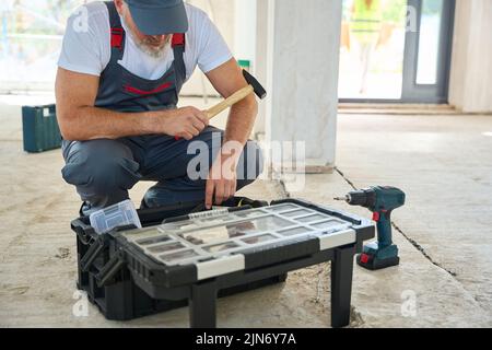 Constructeur barbu avec marteau dans sa main, regardant dans la boîte à outils Banque D'Images