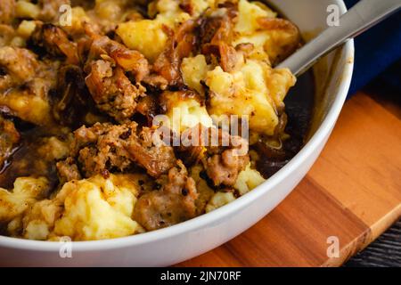 Gros plan de la version déstructurée de Bangers and Mash Wit Stout et sauce à l'oignon : purée de pommes de terre nappée de morceaux de saucisse irlandaise, d'oignons et de sauce Banque D'Images