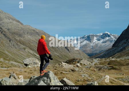 Vue arrière d'un touriste en veste rouge et caméra debout avec vue sur le col Julier, Suisse Banque D'Images