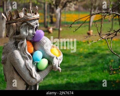 Statue de dame en pierre avec couronne rouillée contenant des œufs de Pâques colorés Banque D'Images