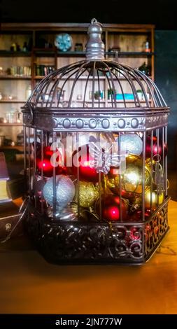 Cage métallique et métallique pleine d'ornements et de lumières de Noël sur un fond sombre de pièce floue avec des étagères et à côté des livres sur une table Banque D'Images