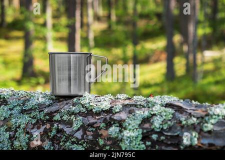 Mug touristique en métal avec boissons chaudes sur le tronc d'arbre dans la forêt. Banque D'Images