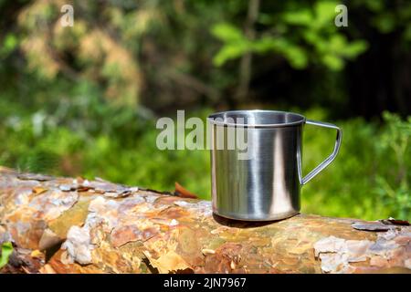 Mug touristique en métal avec boissons chaudes sur le tronc d'arbre dans la forêt. Banque D'Images