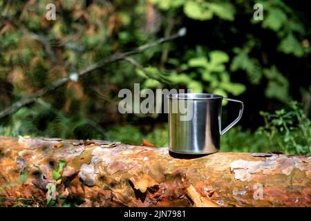 Mug touristique en métal avec boissons chaudes sur le tronc d'arbre dans la forêt. Banque D'Images