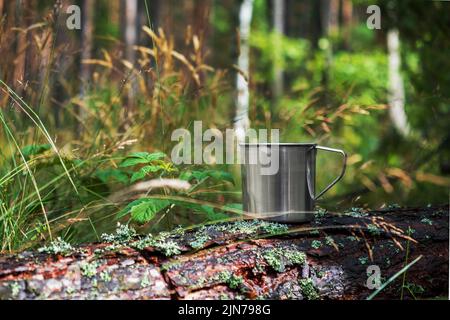 Mug touristique en métal avec boissons chaudes sur le tronc d'arbre dans la forêt. Banque D'Images