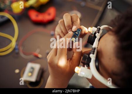 Vue de dessus gros plan d'un garçon noir tenant la carte de circuit imprimé pendant la construction du robot, espace de copie Banque D'Images