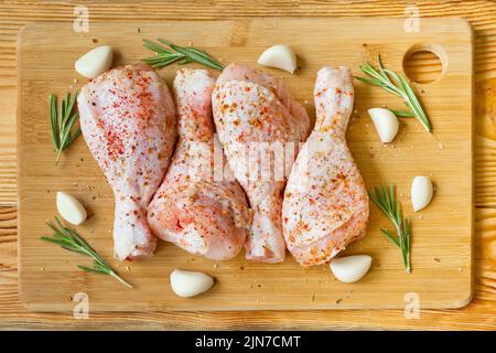 Cuisses de poulet crues marinées avec des épices, de l'ail et du romarin sur une planche à découper en bois. Vue de dessus. Banque D'Images