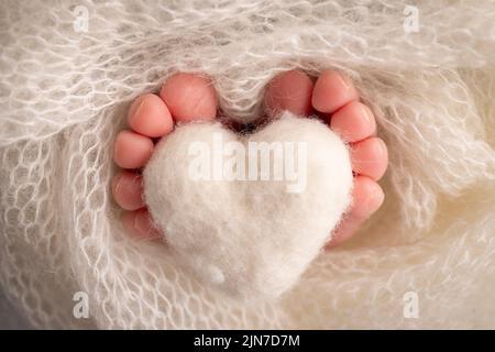 Coeur blanc tricoté dans les jambes d'un bébé. Pieds doux d'un nouveau-né dans une couverture de laine blanche. Banque D'Images