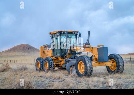 Fort Collins, CO, États-Unis - 31 mars 2022: Niveleuse Deere 770D sur les contreforts du Colorado utilisée pour l'entretien des routes de terre, paysage du début du printemps au crépuscule. Banque D'Images