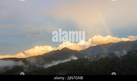 Un coucher de soleil avec un arc-en-ciel et de grands nuages dans le parc national des Great Smoky Mountains. La fumée persiste dans les montagnes après une tempête violente. Banque D'Images