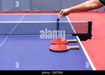 Mesurer le filet de tennis de table en procéder de l'arbitre avant de commencer la compétition entre les joueurs. Il y a deux raquettes sur la table à côté. Banque D'Images