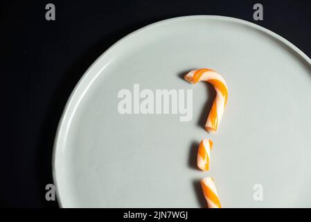 Halloween concept, canne en sucre à rayures orange et blanc cassé sur une assiette. Conception avec arrière-plan noir et espace de copie. Banque D'Images