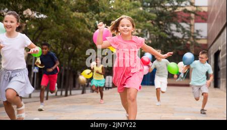 Jeunes filles et garçons joyeux avec des ballons qui s'exécutent dans la rue de la ville Banque D'Images