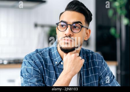 Gros plan d'un sérieux jeune indien ou arabe moderne avec des lunettes, avec une barbe, élégamment habillée, étudiant, indépendant, Spécialiste INFORMATIQUE, regarder, penser, planifier, rêver Banque D'Images