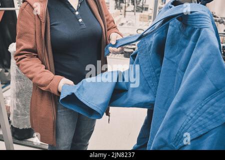 La femme en magasin choisit d'acheter un kimono bleu pour la lutte. Gros plan des mains Banque D'Images