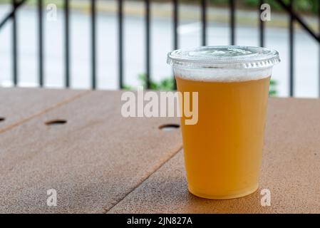 Grand verre en plastique transparent de bière artisanale aigre dans une microbrasserie. Le rafraîchissement froid a du givre sur le verre. La bière est sur une table en bois. Banque D'Images