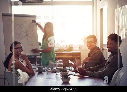 Une heureuse femme d'affaires qui écrit sur le tableau pour expliquer des idées et des pensées tout en remue-méninges avec des collègues. Portrait de divers collègues Banque D'Images