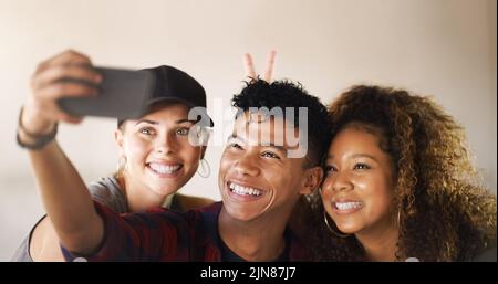 Mais tout d'abord, le lemme prend un selfie. Un jeune groupe varié de danseurs debout contre un fond clos et souriant pour un selfie. Banque D'Images
