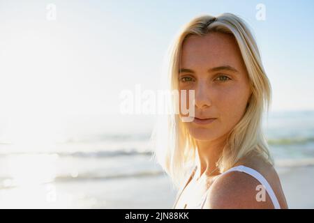 En paix avec moi. Portrait court d'une jeune femme attrayante regardant par-dessus son épaule sur la plage avec l'océan derrière elle. Banque D'Images