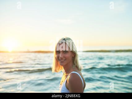 Dans le besoin désespéré de vitamine mer. Portrait court d'une jolie jeune femme souriant sur son épaule sur la plage au coucher du soleil. Banque D'Images