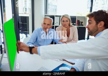 Les résultats de mes tests montrent que c'est la zone infectée. Un médecin discutant des résultats sur son ordinateur avec un homme âgé et sa fille à la clinique. Banque D'Images