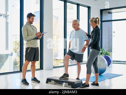 Chaque session a été une marche de progrès. Prise de vue en longueur de deux physiothérapeutes sympathiques travaillant avec un patient âgé. Banque D'Images