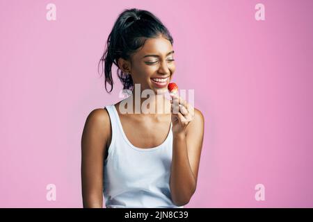 Shes appréciant cette fraise. Photo studio d'une belle jeune femme mangeant une fraise sur fond rose. Banque D'Images