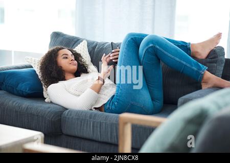 Quel serait le week-end sans mon temps. Une jeune femme utilisant son téléphone portable tout en se relaxant à la maison. Banque D'Images