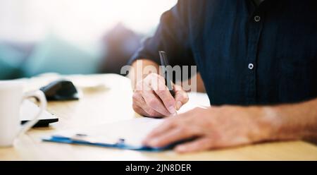 En prenant tous les détails importants, un homme d'affaires méconnaissable écrit quelques notes sur un presse-papiers dans son bureau. Banque D'Images