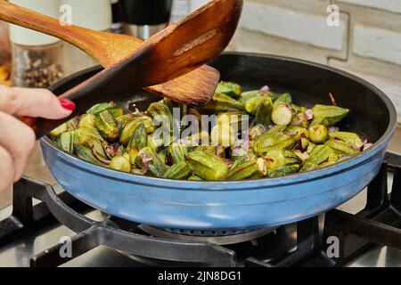 Le chef mélange l'okra dans la poêle avec les oignons violets frits Banque D'Images
