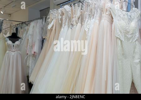 Robes de mariage blanches et crème sur un cintre dans une boutique de mariée. Gros plan. Banque D'Images