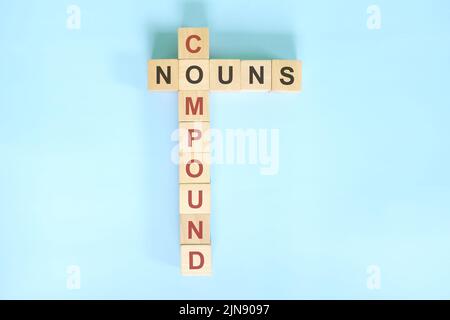 Concept composé de noms dans l'enseignement de grammaire anglaise. Jeu de mots croisés en bois posé sur fond bleu. Banque D'Images