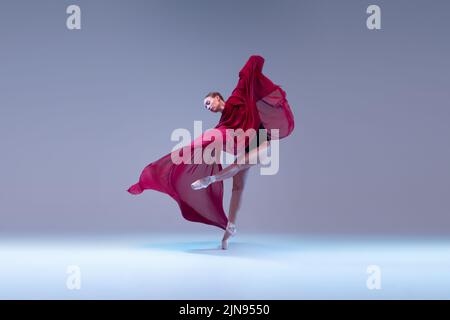 Portrait de la jeune ballerine dansant avec un tissu rouge foncé transparent isolé sur fond bleu gris studio. Grâce Banque D'Images