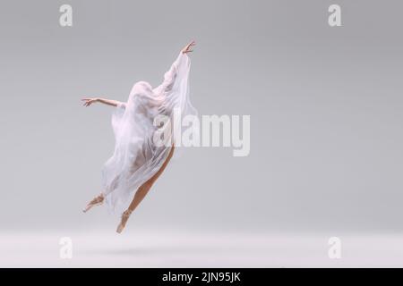 Portrait de la jeune ballerine dansant entièrement recouvert de tissu isolé sur fond gris de studio. La fuite des rêves Banque D'Images