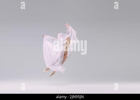 Portrait de la jeune ballerine dansant, en tissu beige, recouvert de tissu isolé sur fond gris studio Banque D'Images