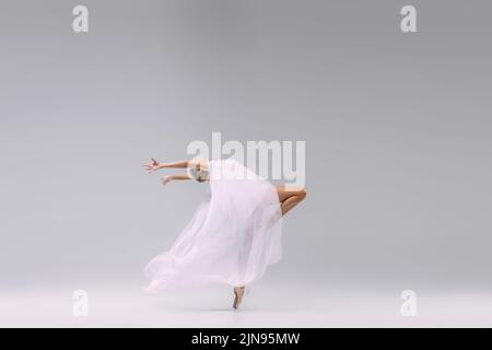 Portrait de la jeune ballerine dansant avec tissu isolé sur fond gris studio. Entièrement recouvert d'un chiffon transparent Banque D'Images