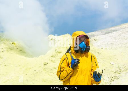 femme volcano scientifique avec un marteau géologique et un échantillon d'un minéral contre le fond d'un fumarale sur la pente d'un volcan Banque D'Images
