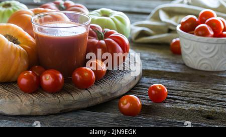 Jus de tomate entouré de tomates à l'ancienne et de tomates cerises, sur un panneau rustique. Banque D'Images