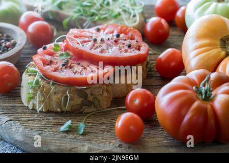 Pain de graines de citrouille recouvert de pousses micro-vertes et de tomates à l'ancienne. Banque D'Images