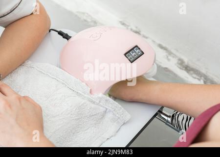 latina la main de fille à l'intérieur d'une lampe à ongles led de 48 watts pour le gel acrylique semi permanent. femme obtenant une manucure pour ses soins de ongles personnels. beauté et vani Banque D'Images