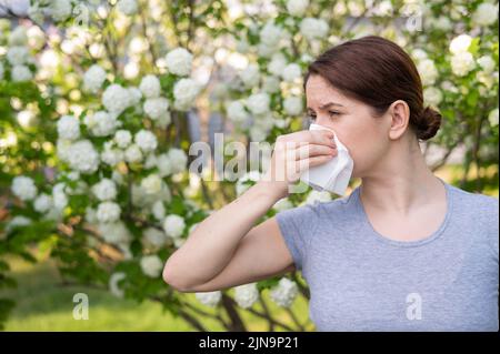 Femme d'âge moyen soufflant son nez dans un jardin fleuri. Banque D'Images