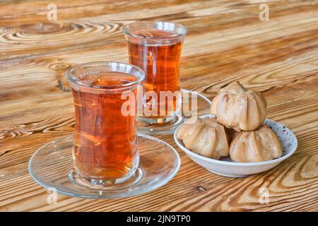 Deux tasses traditionnelles en verre turc de thé noir avec des profiteroles sucrées sur une table en bois. Petit déjeuner pour deux personnes. Mise au point sélective. Banque D'Images