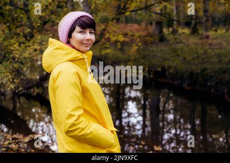 Portrait de femme souriante en imperméable jaune vif sur le fond de la rivière à la forêt, en profitant du moment. Sensation d'harmonie, réunion avec n Banque D'Images