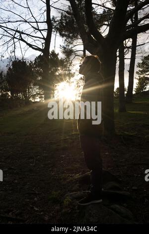 adolescent dans la forêt au coucher du soleil avec des rayons du soleil qui brillent parmi les arbres Banque D'Images