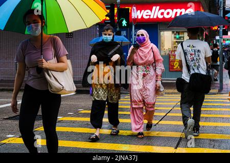 Hong Kong, Chine. 10th août 2022. Les gens portent un masque facial et des parasols traversent une rue sous la pluie. (Image de crédit : © Keith Tsuji/ZUMA Press Wire) Banque D'Images