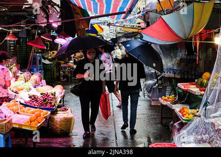 Hong Kong, Chine. 10th août 2022. Les gens portent un masque facial et des parasols traversent une rue sous la pluie. (Image de crédit : © Keith Tsuji/ZUMA Press Wire) Banque D'Images