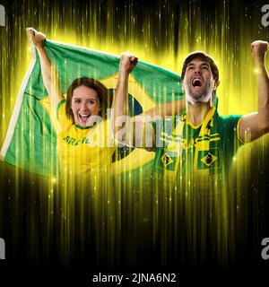 Couple brésilien célébrant la coupe sur un fond noir avec une lueur jaune, encourageant le Brésil à être le champion. Banque D'Images