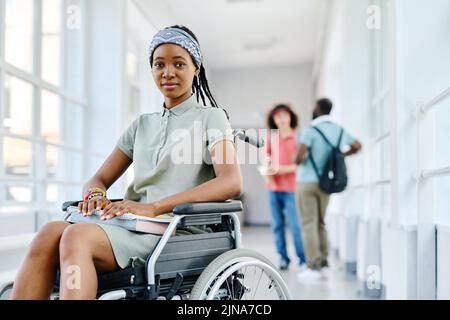 Portrait d'une adolescente africaine assise en fauteuil roulant et regardant un appareil photo pendant une pause à l'école Banque D'Images