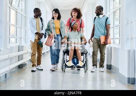 Fille africaine en fauteuil roulant discutant avec ses amis pendant qu'ils marchent le long du couloir de l'école Banque D'Images