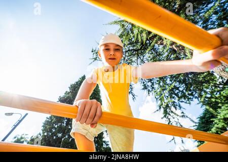 Joyeux garçon grimpant sur un cadre d'escalade dans un parc en été, Géorgie Banque D'Images